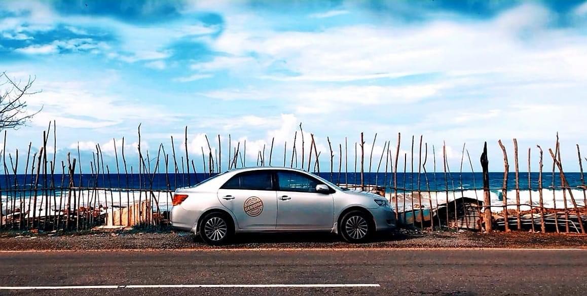 Private tour car on a Sri Lankan coastal road with the Indian Ocean beyond a wooden fence